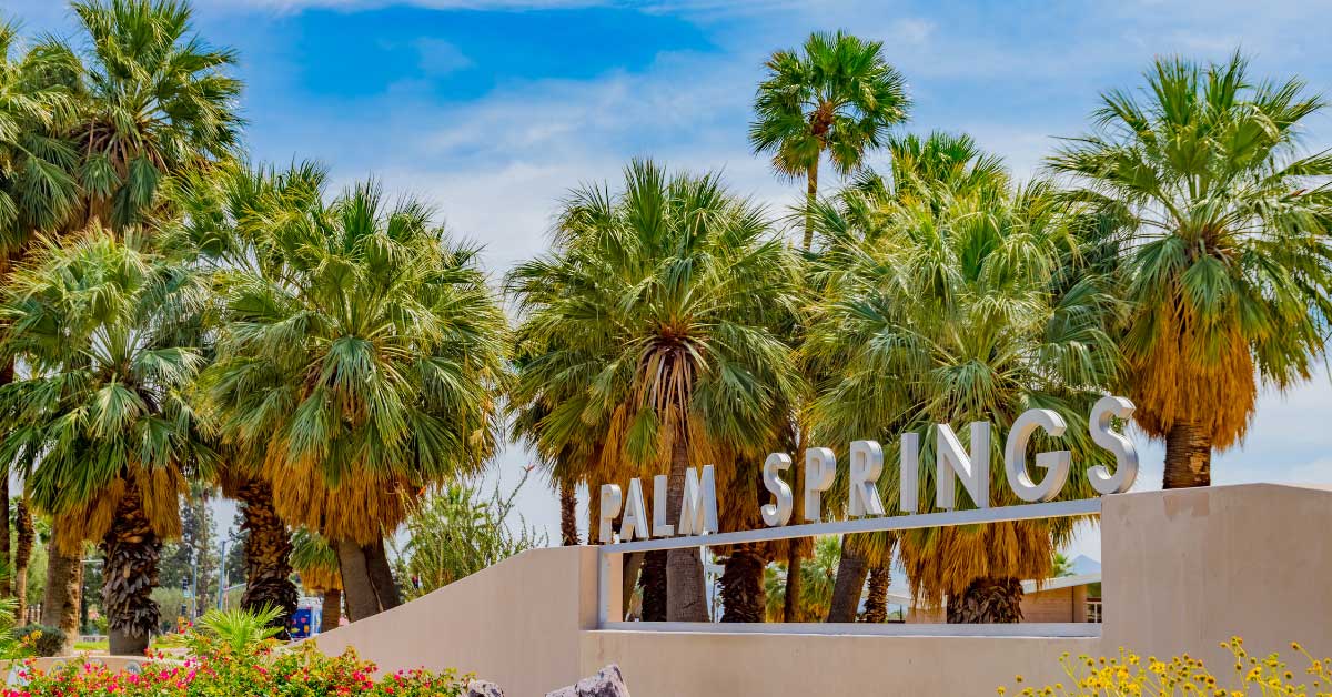 City sign spelling out Palm Springs against a blue sky and palm trees