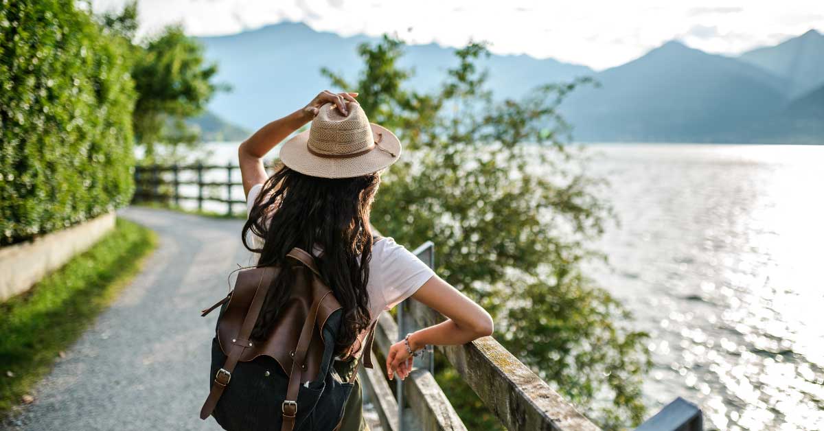 back of woman overlooking ocean wearing backpack and hat