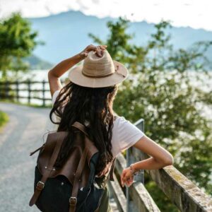 back of woman overlooking ocean wearing backpack and hat