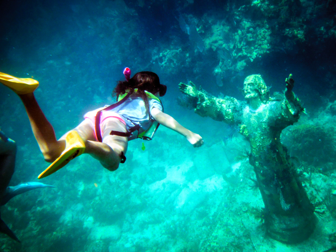 Underwater shot of a young girl snorkeling to the Christ of the Abyss Statue off Key Largo Florida Gulf of Mexico with fish swimming around and plant life growing.